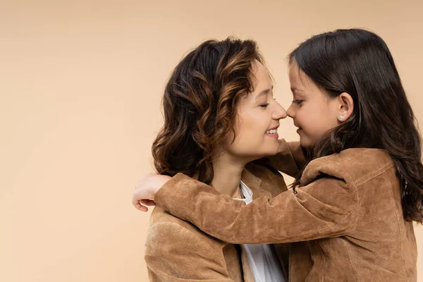 Vista laterale del bambino che abbraccia la mamma felice in giacca scamosciata marrone isolata sul beige — Foto stock