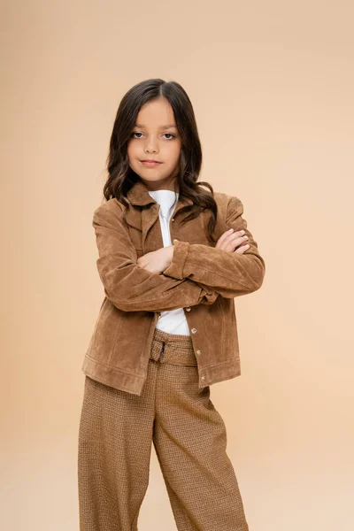 Child in trendy autumn jacket and pants standing with crossed arms isolated on beige — Stock Photo