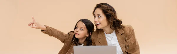 Ragazza alla moda che punta con il dito vicino al computer portatile e mamma stupita isolata sul beige, banner — Foto stock