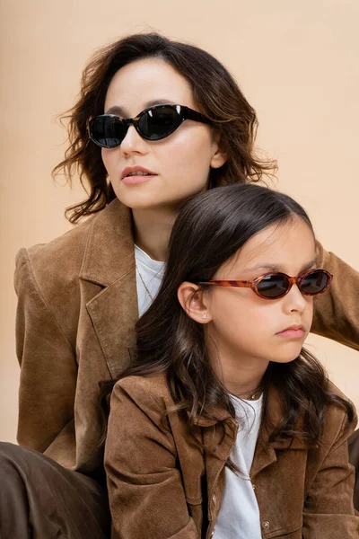 Trendy mother and daughter in sunglasses and brown suede jackets isolated on beige — Stock Photo