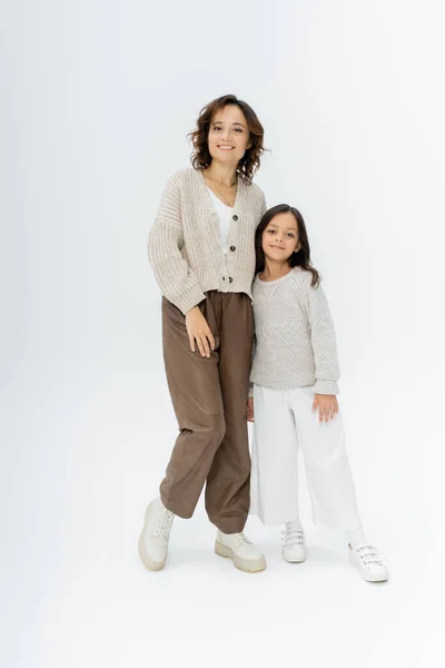 Pleine longueur de mère et fille en tricot et pantalon posant sur fond gris — Photo de stock