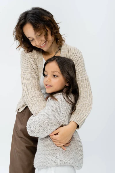 Щаслива брюнетка з дочкою в теплому трикотажі, що обіймається ізольовано на сірому — стокове фото