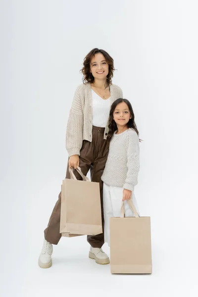 Жінка і дівчина в модному осінньому одязі тримає сумки для покупок і дивиться на камеру на сірому фоні — стокове фото