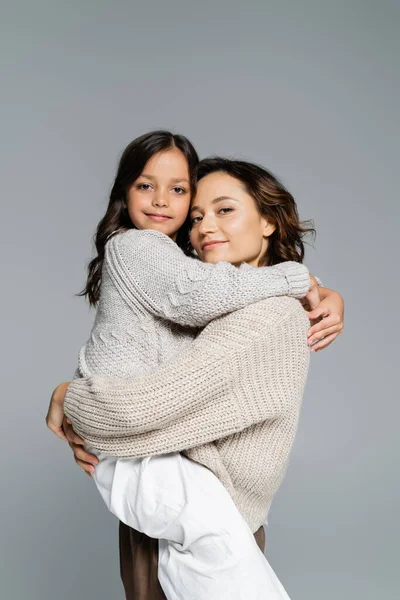 Femme heureuse et fille souriante en tricot élégant étreignant et regardant la caméra isolée sur gris — Photo de stock