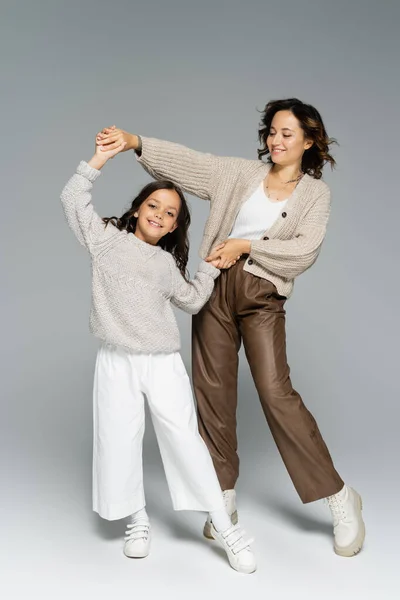 Excited mother and child in autumn clothes holding hands and dancing on grey background — Stock Photo