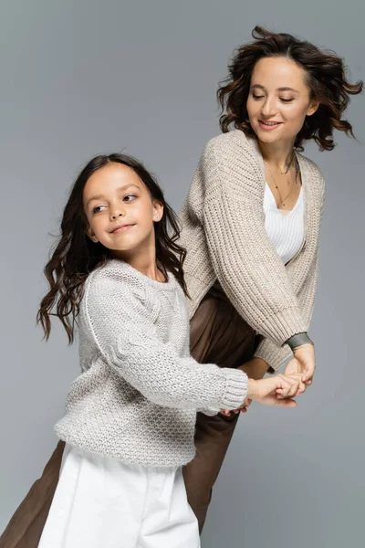 Happy mother and daughter in autumn clothes holding hands while dancing isolated on grey — Stock Photo