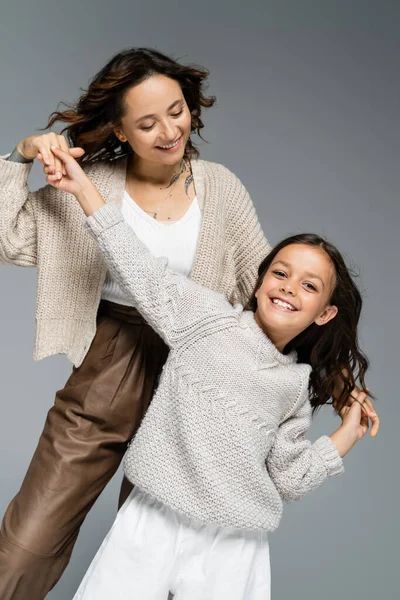 Trendy and cheerful girl looking at camera while dancing with happy mom isolated on grey — Stock Photo