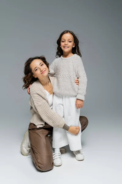 Feliz madre e hijo en ropa elegante y cálida posando sobre fondo gris - foto de stock