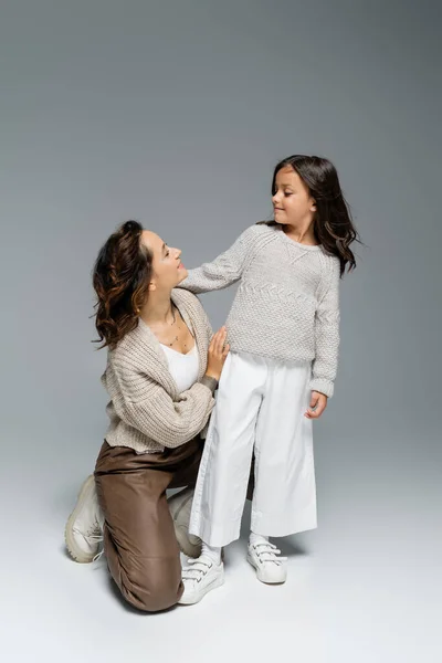 Mujer y chica en punto y pantalones de moda mirándose el uno al otro sobre fondo gris - foto de stock