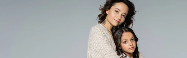 Brunette woman and girl in knitwear looking at camera isolated on grey, banner — Stock Photo