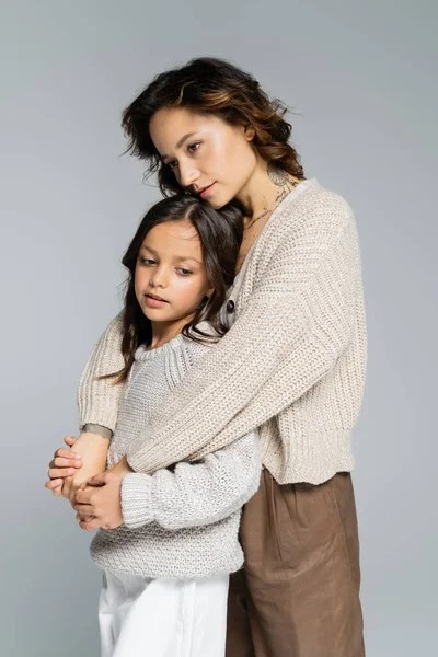 Dreamy woman in trendy autumn clothes hugging daughter isolated on grey — Stock Photo