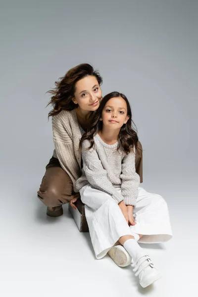 Mujer y niño en traje de otoño de moda mirando a la cámara mientras está sentado sobre fondo gris - foto de stock