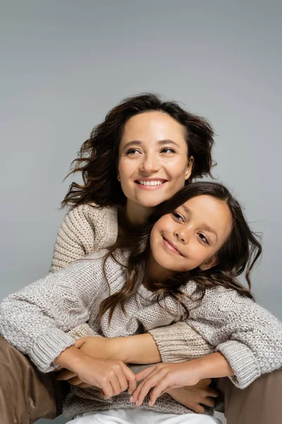 Joyeuse mère et enfant en vêtements chauds d'automne embrassant et regardant loin isolé sur gris — Photo de stock