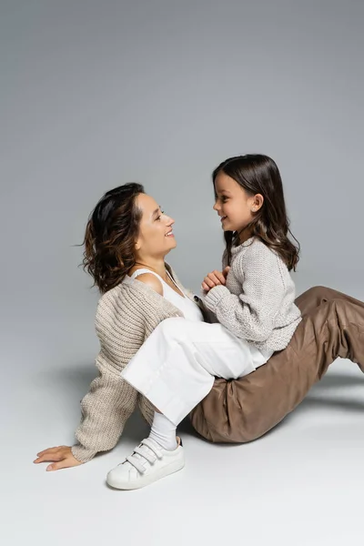Seitenansicht von glücklicher Mutter und Kind in warmer Kleidung, die sich auf grauem Hintergrund anschauen — Stockfoto