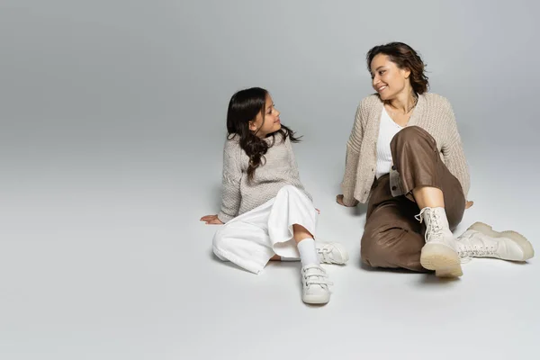 Modische Mutter und Tochter lächeln einander auf grauem Hintergrund an — Stockfoto