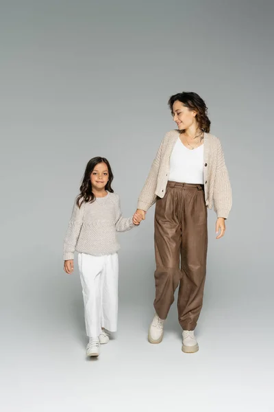 Улыбающаяся женщина в стильной осенней одежде гуляет с дочерью на сером фоне — стоковое фото