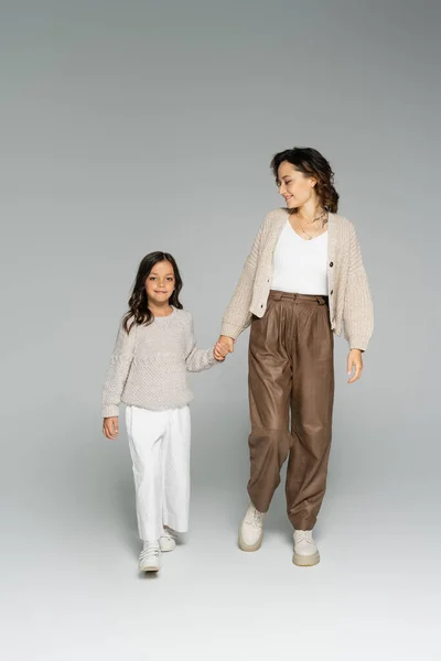 Femme souriante dans des vêtements d'automne élégants marchant avec fille sur fond gris — Photo de stock