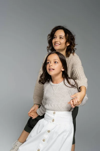 Happy mom and child in warm knitwear holding hands and looking away isolated on grey — Stock Photo