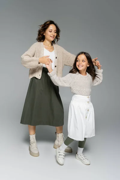 Longitud completa de mujer y niña en faldas cogidas de la mano y bailando sobre fondo gris - foto de stock