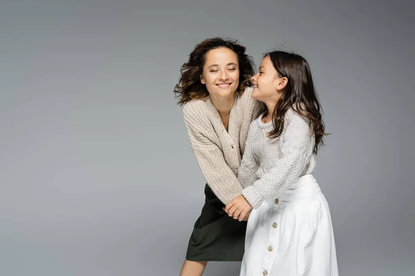 Excited brunette woman with closed eyes holding hands with stylish daughter isolated on grey — Stock Photo