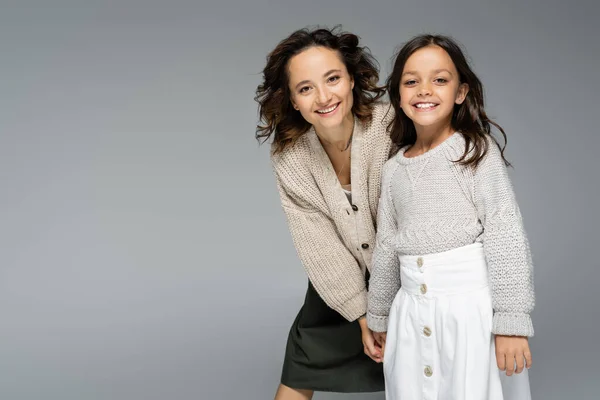 Gioiosa donna e ragazza in abito alla moda e caldo che si tiene per mano e posa isolata sul grigio — Foto stock