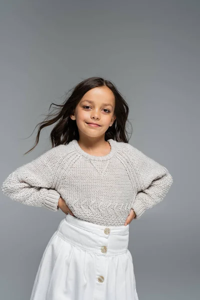 Fille à la mode en pull tricoté et jupe blanche posant avec les mains sur les hanches isolées sur gris — Photo de stock