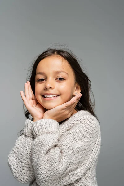 Excited child in warm sweater holding hands near face and looking at camera isolated on grey — Stock Photo