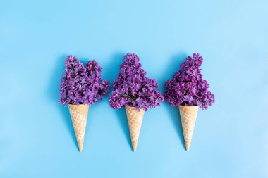 Mavi arka planda bir buket leylak olan üç waffle fincanı..