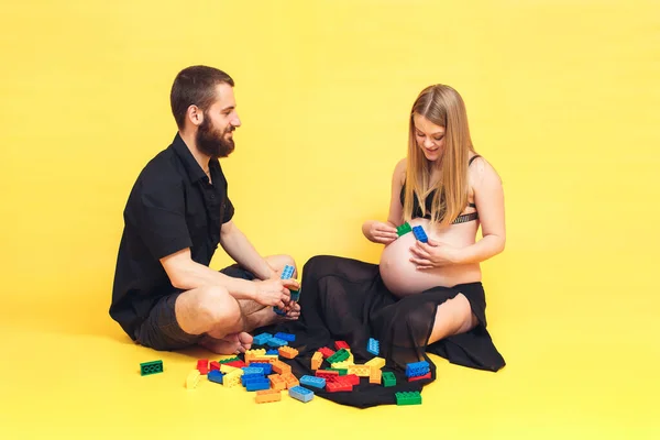 Marido e mulher jogar criança construtor. uma menina grávida coloca o designer em seu estômago. — Fotografia de Stock