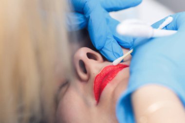 Kadın kozmetoloji salonunda kalıcı makyaj yapıyor. Dudak hatları çiziyor..