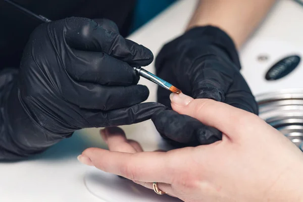 Manicurist paints nails with gel polish. Applying acrylic nail lacquer. Manicure service. The specialist covers the clients nail with a transparent gel. — Stockfoto