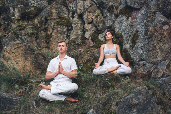 a young couple meditates sitting in a lotus position on a rock