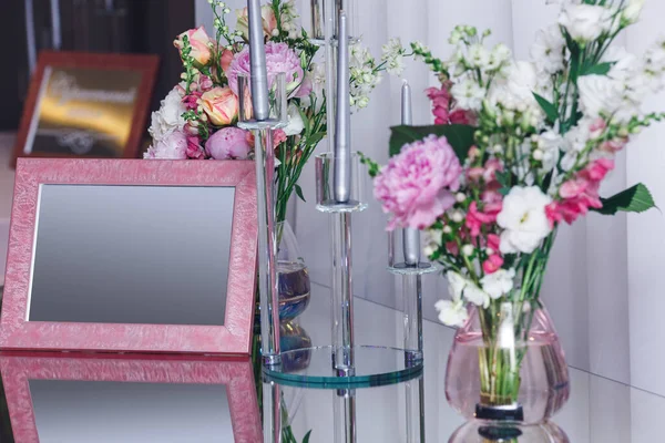 pink empty frame and flowers in a vase on a mirror table