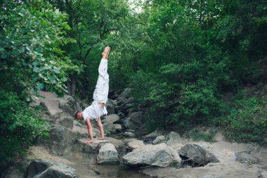 a young guy is doing yoga in nature, performing a handstand