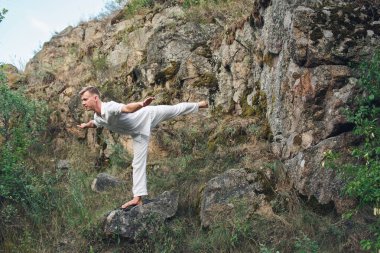 Genç bir adam kayanın yanında yoga yapıyor.