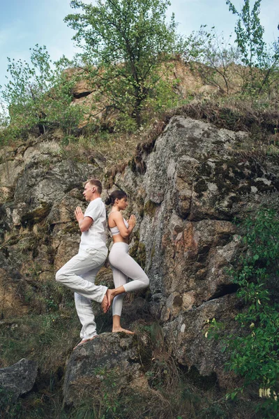 a young couple meditates in nature near a rock