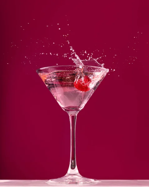 Raspberry splash in a martini cocktail glass on dark red background