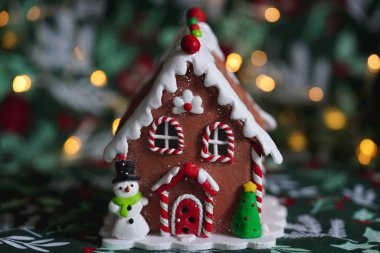 Zencefilli kurabiye evi Noel süslemesi, kardan adam ve arka planda festival ışıkları olan Noel ağacı.