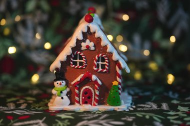 Zencefilli kurabiye evi Noel süslemesi, kardan adam ve arka planda festival ışıkları olan Noel ağacı.