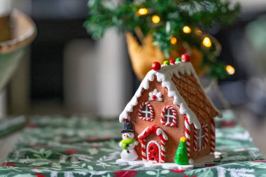 Zencefilli kurabiye evi Noel süslemesi, kardan adam ve arka planda festival ışıkları olan Noel ağacı.