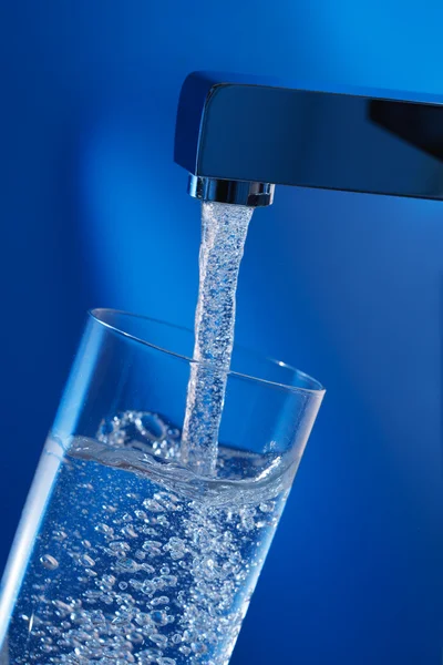 Een glas water te vullen. blauwe achtergrond. — Stockfoto