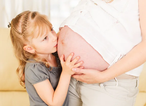 Mädchen küsst Schwangerschaftsbauch ihrer Mutter. — Stockfoto