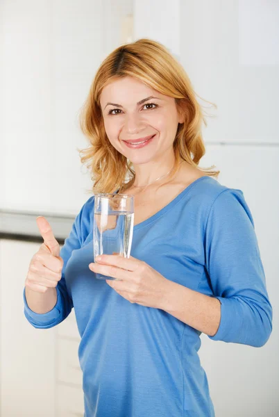 Schöne Frau hält ein Glas Wasser und zeigt Daumen nach oben s — Stockfoto