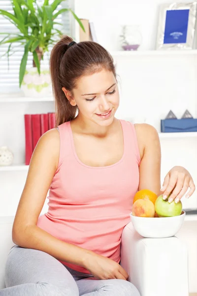 Mulher feliz em casa no sofá com frutas — Fotografia de Stock