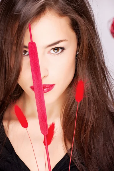 Hübsche Frau mit langen Haaren hinter roter Pflanze — Stockfoto