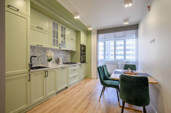 Modern trendy light green luxurious kitchen with dining table and dark green chairs