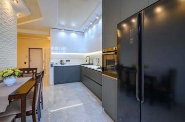 Geniş lüks, beyaz ve koyu gri mutfak. Yemek masası var.