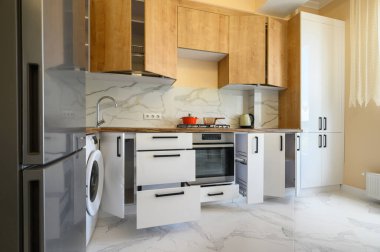 Modern white and wooden furniture in yellow kitchen with yellow walls and white marble floor, some drawers and doors are open