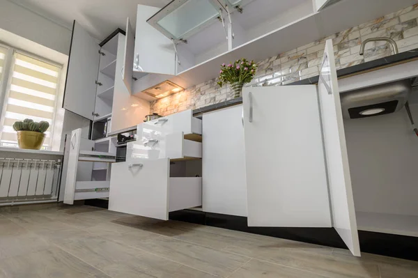 Interior renovation showcase of well designed modern trendy white kitchen, cabinet doors open, drawers retracted, low angle view