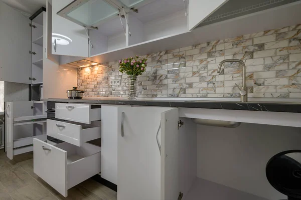 Interior renovation showcase of well designed modern trendy white kitchen, cabinet doors open, drawers retracted